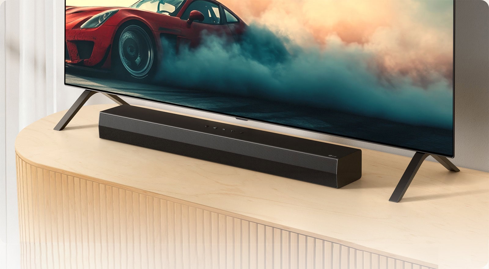 Το LG Soundbar S20A τοποθετείται σε μια ξύλινη κονσόλα τηλεόρασης, κάτω από μια τηλεόραση και ανάμεσα στις βάσεις της τηλεόρασης. Στην τηλεόραση εμφανίζεται ένα κόκκινο αυτοκίνητο με καπνό.