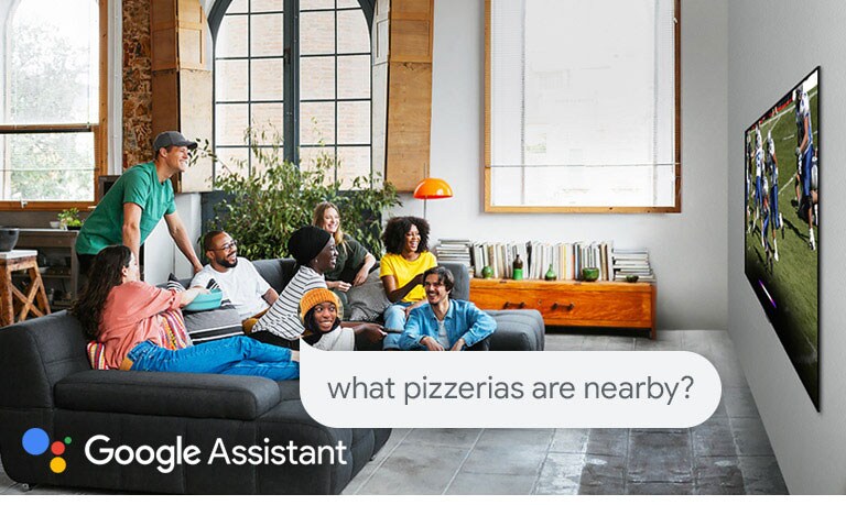 Μια γυναίκα που παρακολουθεί ποδόσφαιρο στην τηλεόραση με φίλους και ρωτά το Google Assistant ποιες πιτσαρίες υπάρχουν κοντά στο σπίτι της