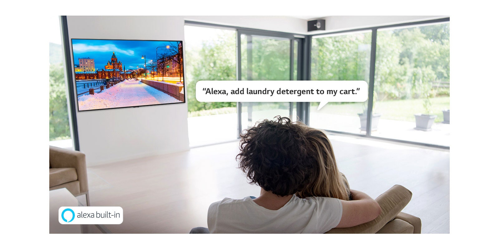 Ένα ζευγάρι που κάθεται στον καναπέ ζητώντας από το Amazon Alexa να προσθέσει απορρυπαντικό πλυντηρίου στο καλάθι αγορών