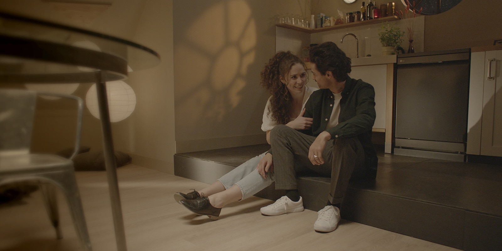 Μπροστά από το πλυντήριο πιάτων, ένα ζευγάρι κάθεται δίπλα-δίπλα χαμογελώντας ο ένας στον άλλον. Αυτή η εικόνα διαδέχεται την άλλη εικόνα. Φαίνεται το εσωτερικό του πλυντηρίου πιάτων, όπου πλένονται τα πιάτα.