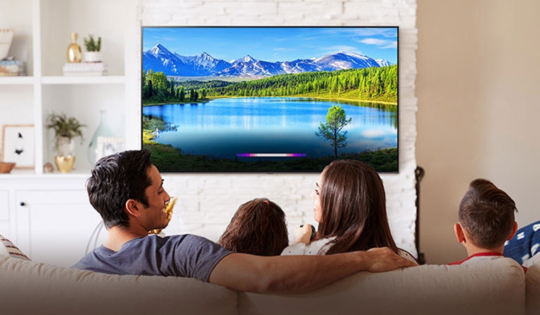 Μια οικογένεια σε ένα φωτεινό σαλόνι που βλέπει ένα τοπίο σε μια τηλεόραση τοποθετημένη στον τοίχο