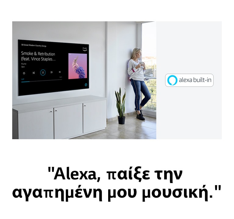 Μια γυναίκα που γέρνει στον τοίχο δίπλα στην τηλεόραση, κοιτάζοντας έξω από το παράθυρο και ζητώντας από την Alexa να παίξει την αγαπημένη της μουσική.