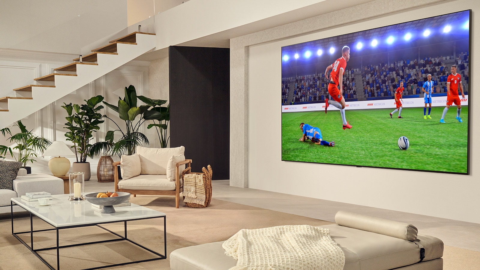 Μια οικογένεια στο σαλόνι. Έχουν μια LG TV επιτοίχιας τοποθέτησης με μια εξαιρετικά μεγάλη οθόνη, η οποία καλύπτει σχεδόν ολόκληρο τον τοίχο. Παρακολουθούν έναν συναρπαστικό αγώνα ποδοσφαίρου στη μεγάλη και καθηλωτική οθόνη.