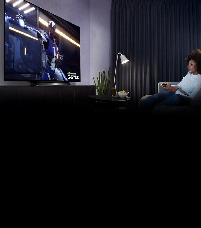 Μία γυναίκα σε ένα καναπέ, κρατάει ένα χειριστήριο ενώ παίζει ένα παιχνίδι στην τηλεόραση