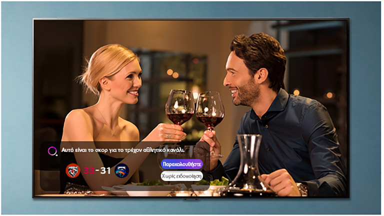 Μια οθόνη τηλεόρασης που απεικονίζει έναν άνδρα και μια γυναίκα που τσουγκρίζουν τα ποτήρια τους, ενώ εμφανίζονται αθλητικές ειδοποιήσεις