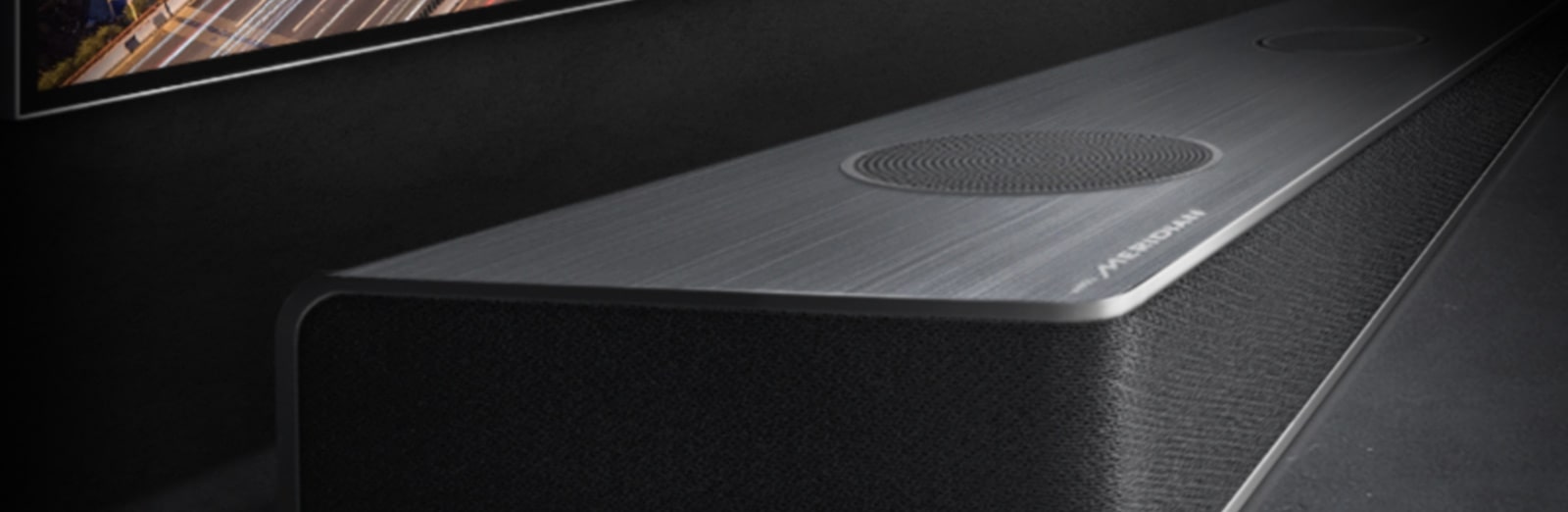 Διακρίνεται η άκρη του soundbar κάτω από την οθόνη της τηλεόρασης με τη νυχτερινή άποψη του δρόμου.