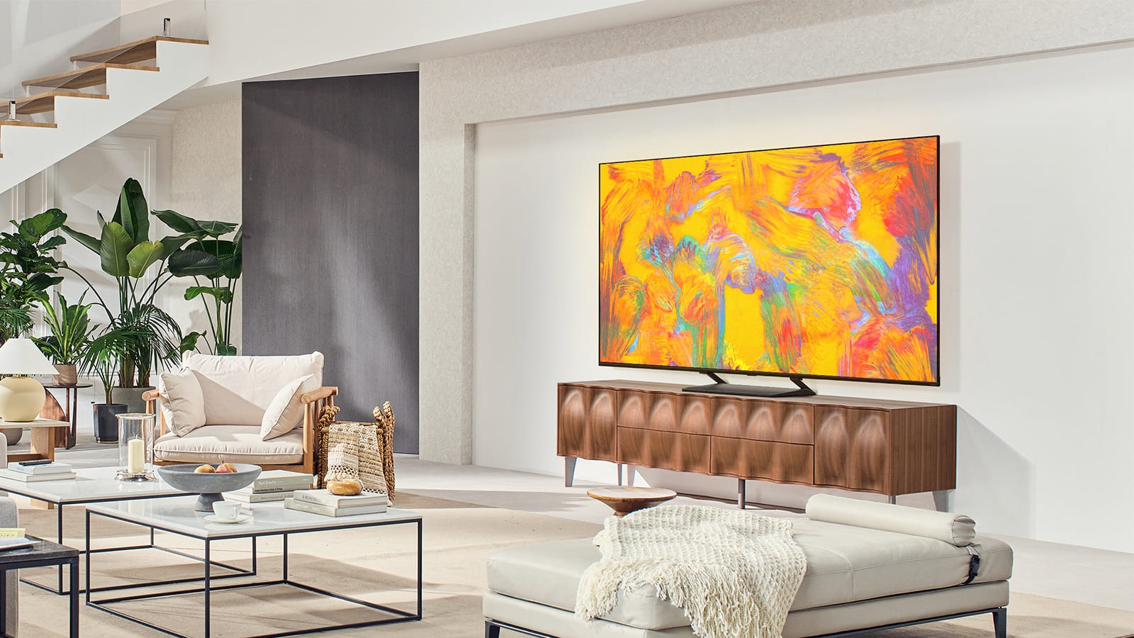 Η LG QNED TV βρίσκεται πάνω από ένα συρτάρι τηλεόρασης σε ένα άνετο σαλόνι. Η LG QNED TV απεικονίζει ένα αφηρημένο φόντο σε πορτοκαλί, κίτρινο, μωβ και ροζ.