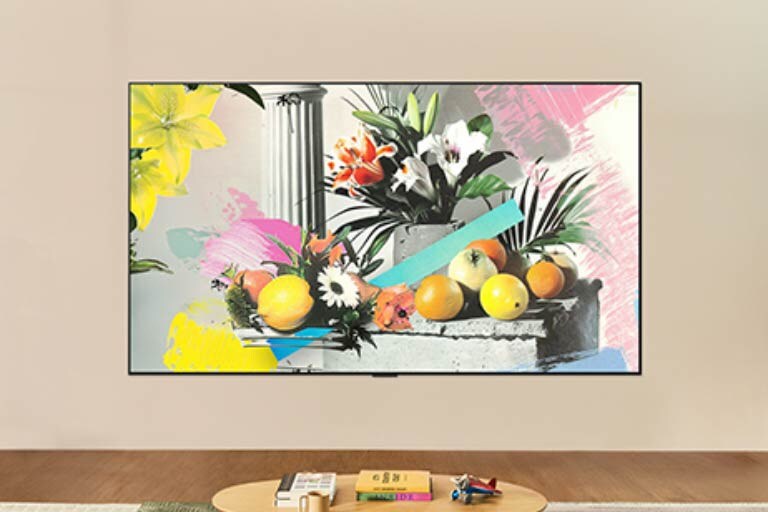 Η LG QNED evo AI QNED82 Mini LED είναι επιτοίχια σε ένα φωτεινό δωμάτιο, δείχνοντας ένα πολύχρωμο έργο τέχνης με λουλούδια και φρούτα στη λειτουργία Gallery, ενώ ο έλεγχος φωτεινότητας προσαρμόζεται για βέλτιστη προβολή σε οποιεσδήποτε συνθήκες φωτισμού. 