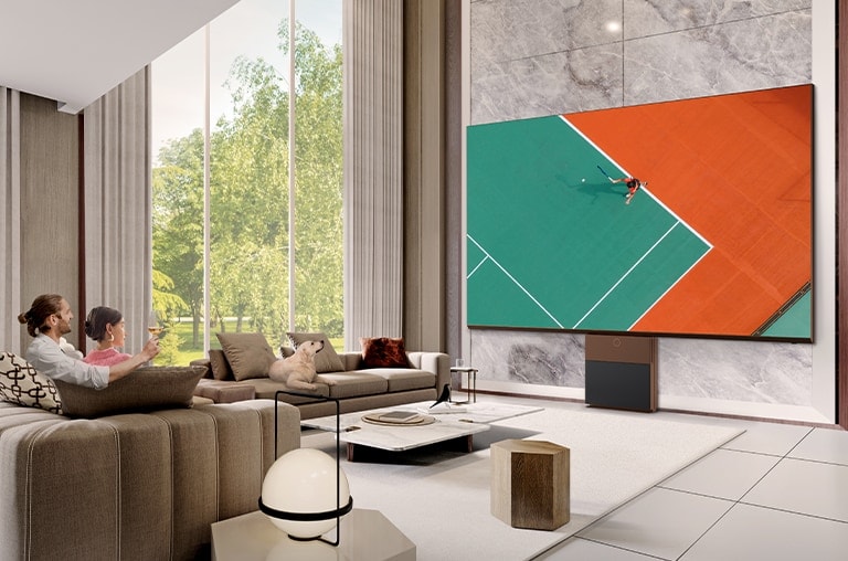 Ένα ζευγάρι παρακολουθεί έναν αγώνα τένις σε μία μεγάλη οθόνη LG MAGNIT μέγιστης υψηλής ευκρίνειας στο σαλόνι.