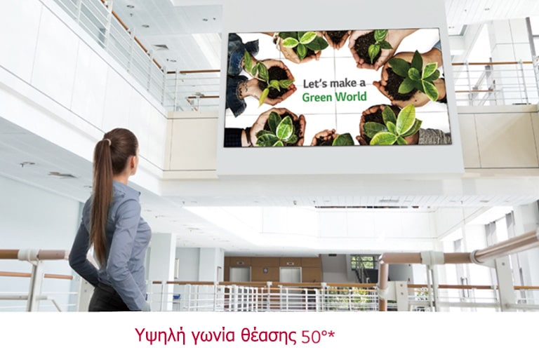 Μια γυναίκα κοιτάζει προς τα πάνω σε μια οθόνη που είναι εγκατεστημένη στον πάνω όροφο.