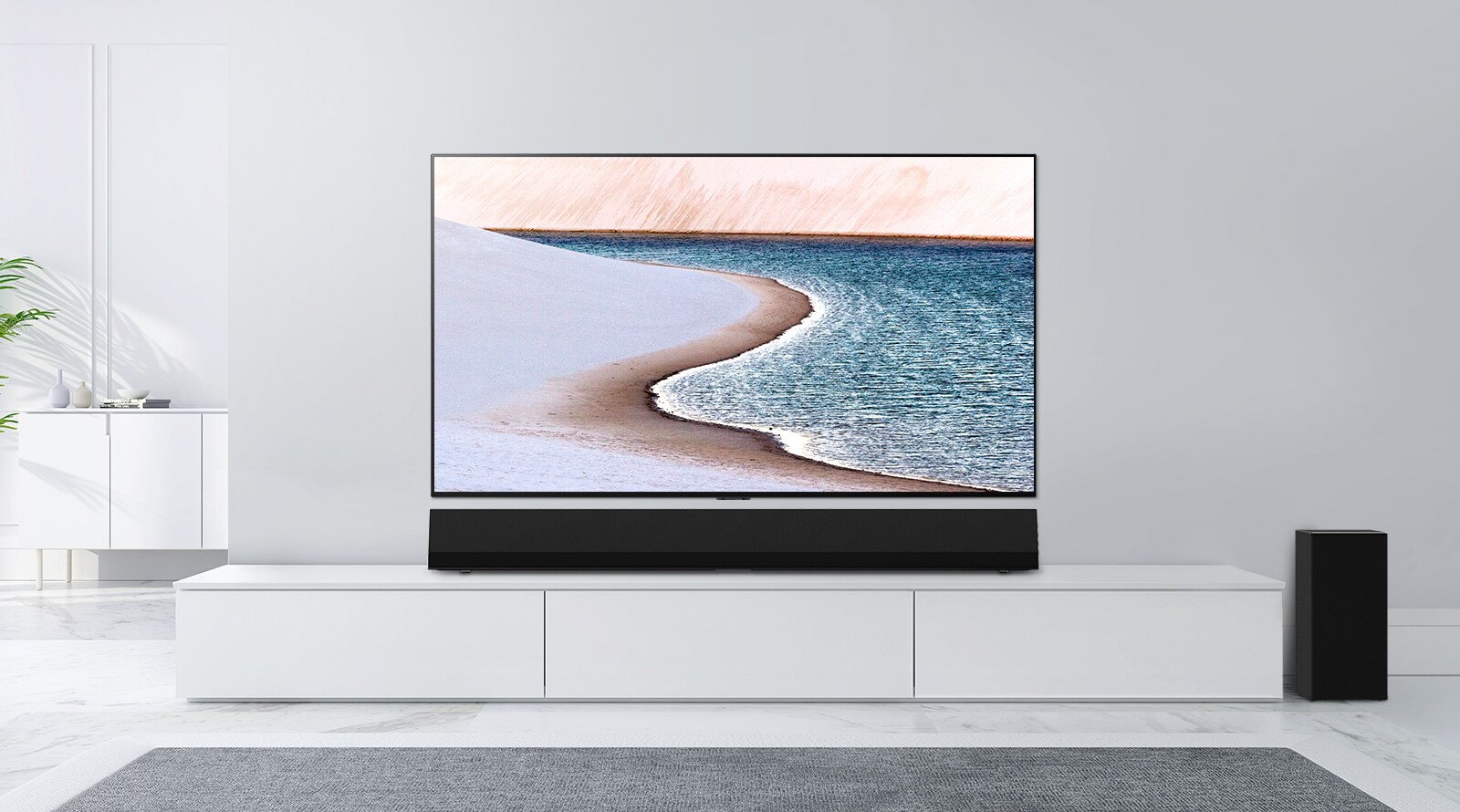 Μια τηλεόραση στερεωμένη σε έναν τοίχο ανοιχτού γκρίζου χρώματος. Το LG Soundbar βρίσκεται από κάτω, επάνω σε ένα λευκό ερμάριο. Η τηλεόραση δείχνει μια παραλία.