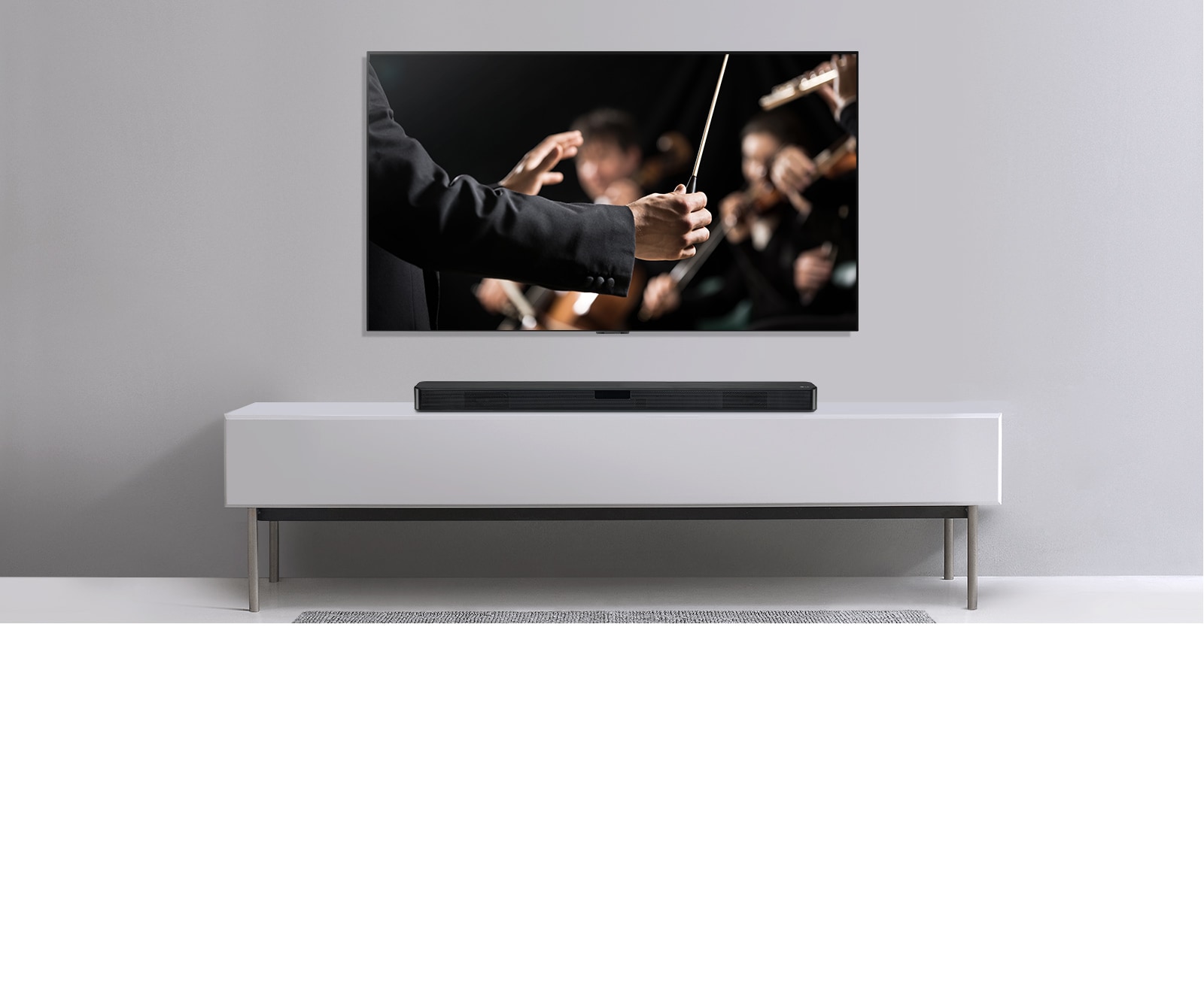 Τηλεόραση σε γκρι τοίχο και κάτω σε ένα γκτι ράφι - ένα LG Sound Bar. Στην τηλεόραση ένας μαέστρος διευθύνει μια ορχήστρα.