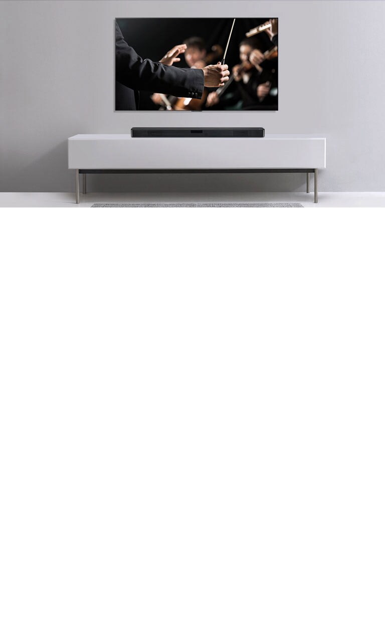 Τηλεόραση σε γκρι τοίχο και κάτω σε ένα γκτι ράφι - ένα LG Sound Bar. Στην τηλεόραση ένας μαέστρος διευθύνει μια ορχήστρα.