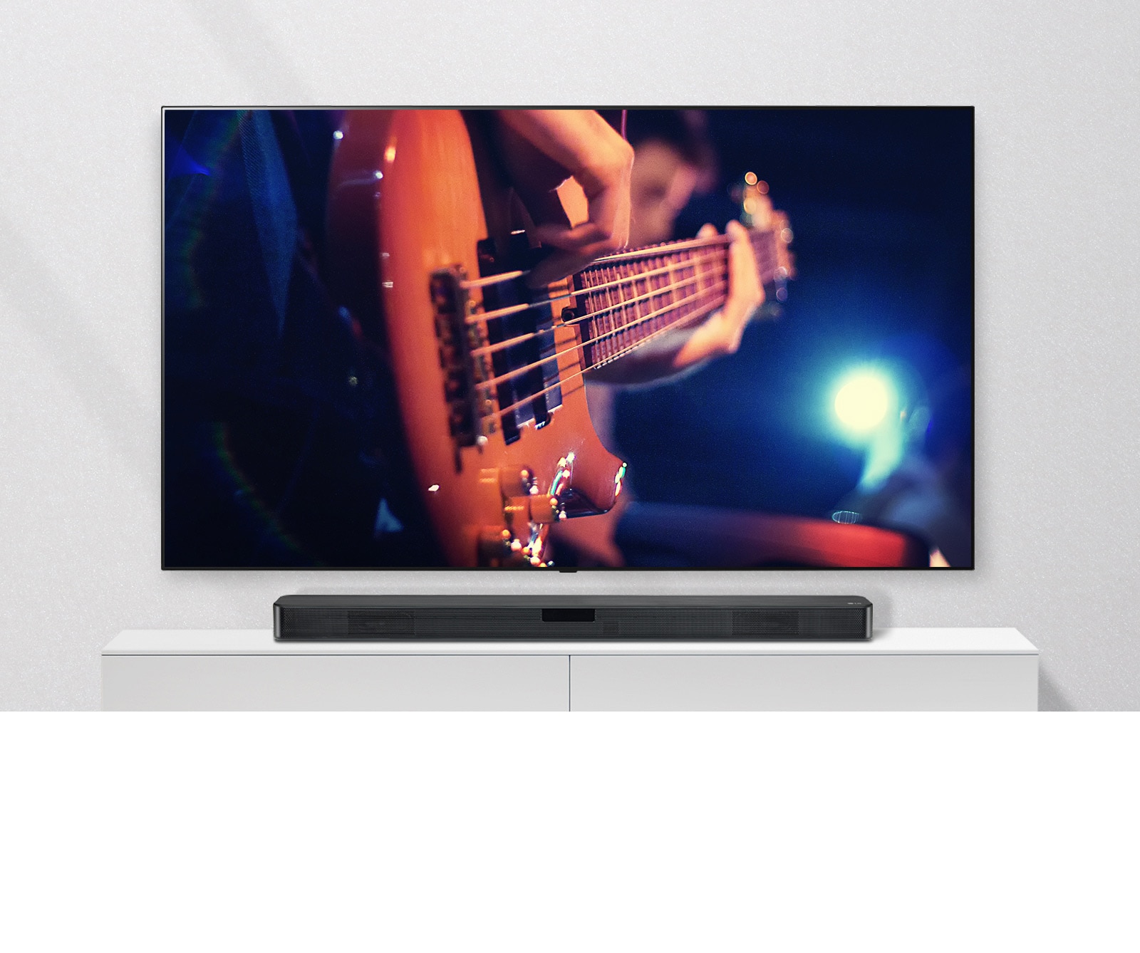 Μια τηλεόραση στον τοίχο με το Sound Bar σε ένα λευκό ράφι. Η τηλεόραση δείχνει έναν άνδρα να παίζει κιθάρα.