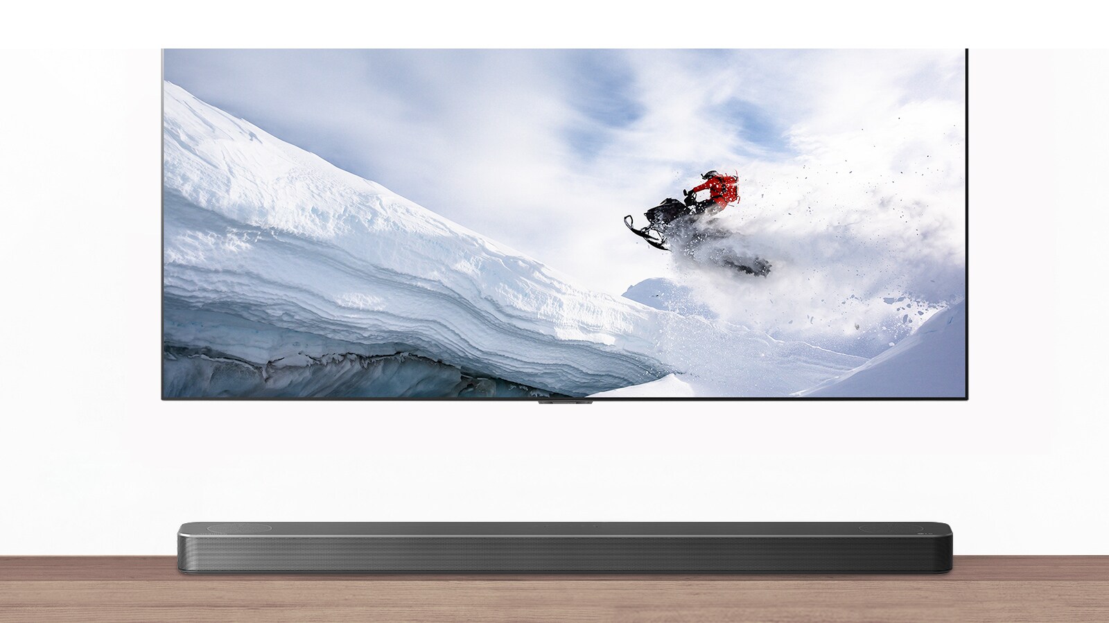 Η τηλεόραση & το Soundbar φαίνονται από εμπρός. Η τηλεόραση δείχνει έναν άντρα επάνω σε ένα όχημα χιονιού σε χιονισμένα βουνά. Το λογότυπο του HDMI 2.1 βρίσκεται κάτω από την τηλεόραση.