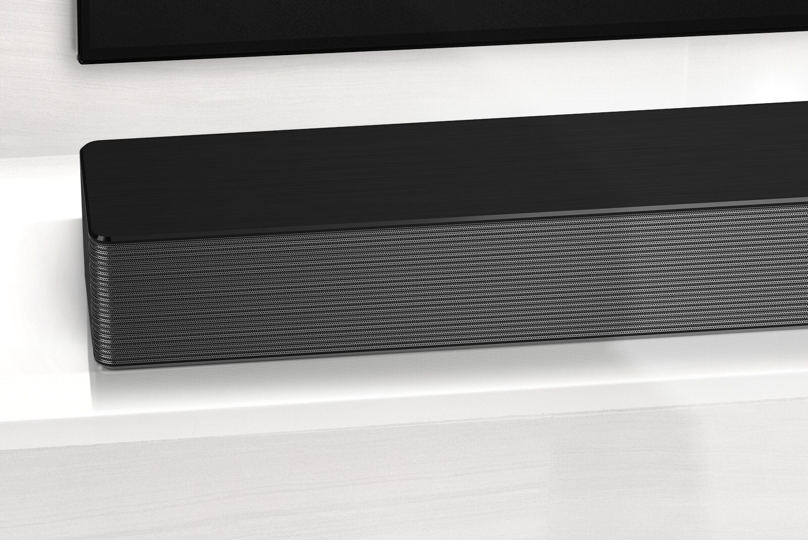 Κοντινό πλάνο του LG Soundbar στην αριστερή του γωνία. Η κάτω αριστερή πλευρά της τηλεόρασης είναι επίσης ορατή.