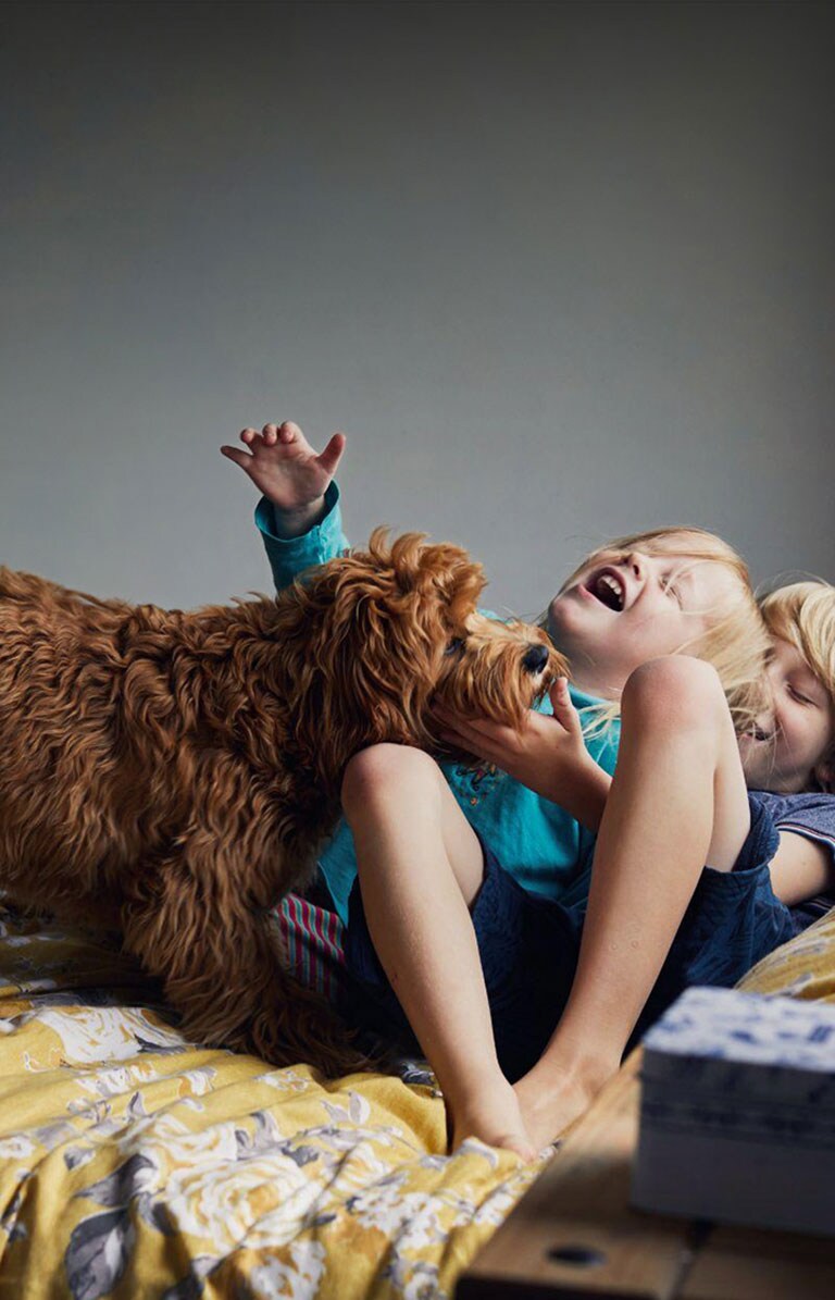 Δύο παιδιά και ένας σκύλος είναι ξαπλωμένα στο κρεβάτι και χαμογελάνε