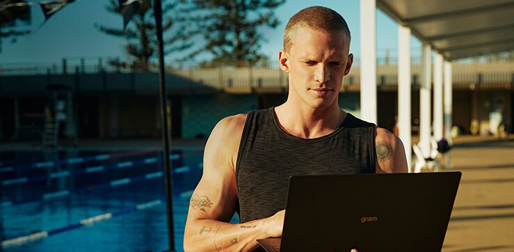 Ο Cody Simpson απολαμβάνει το φως του ήλιοου δίπλα στην πισίνα και χρησιμοποιεί τον φορητό υπολογιστή του.