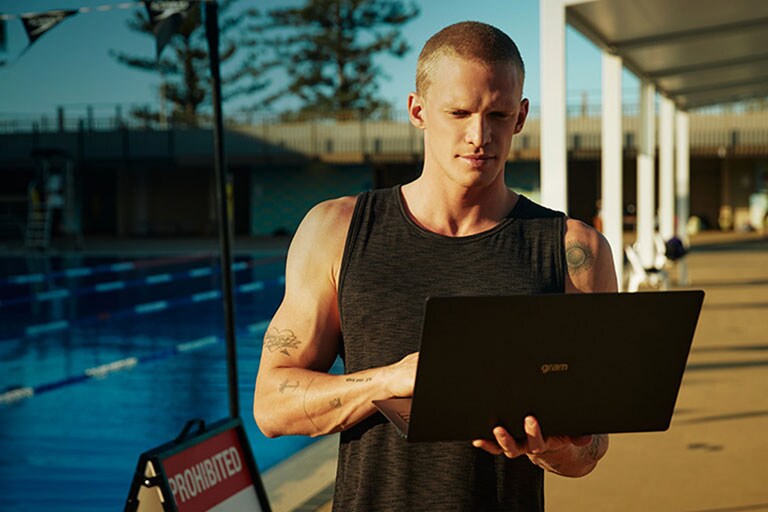 Ο Cody Simpson απολαμβάνει το φως του ήλιοου δίπλα στην πισίνα και χρησιμοποιεί τον φορητό υπολογιστή του.