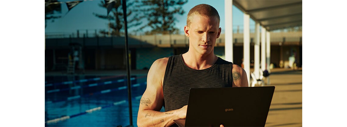 Ο Cody Simpson απολαμβάνει το φως του ήλιοου δίπλα στην πισίνα και χρησιμοποιεί τον φορητό υπολογιστή του.