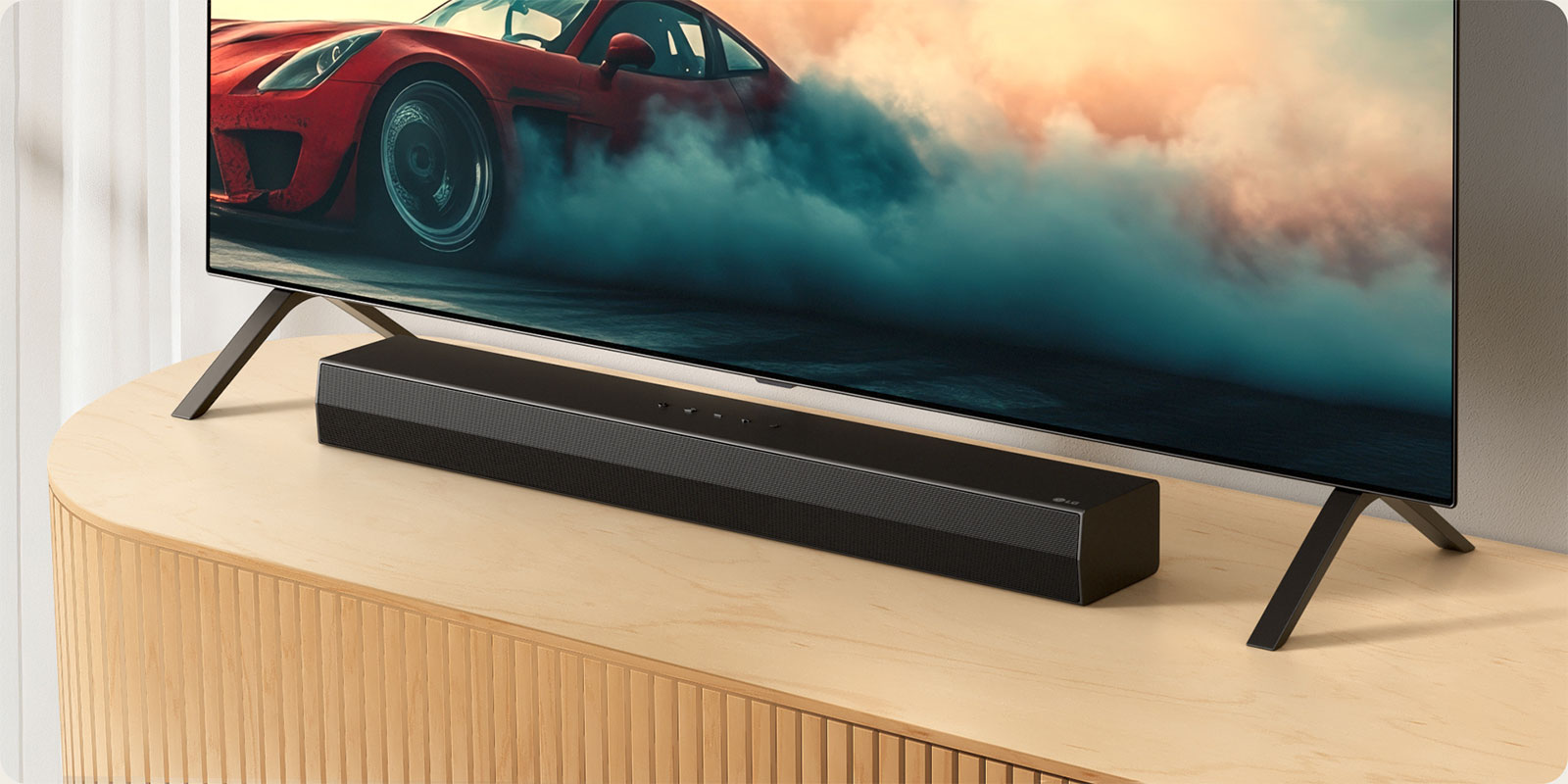 Το LG Soundbar S20A τοποθετείται σε μια ξύλινη κονσόλα τηλεόρασης, κάτω από μια τηλεόραση και ανάμεσα στις βάσεις της τηλεόρασης. Στην τηλεόραση εμφανίζεται ένα κόκκινο αυτοκίνητο με καπνό.