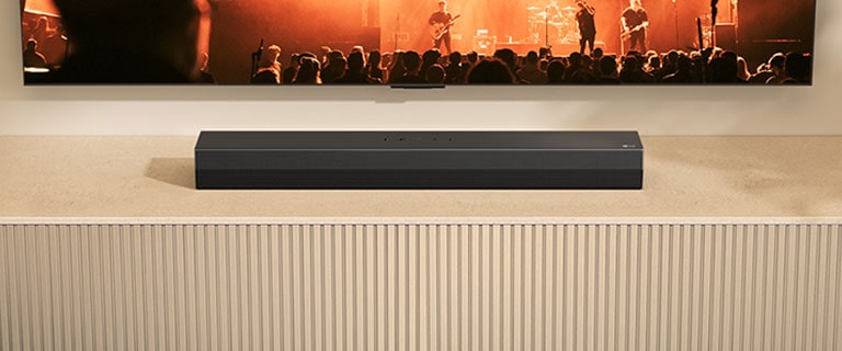 Το S20A soundbar τοποθετείται πάνω σε μια ξύλινη κονσόλα τηλεόρασης. Πάνω από αυτό μια τηλεόραση εμφανίζεται μερικώς με μια σκηνή συναυλίας.