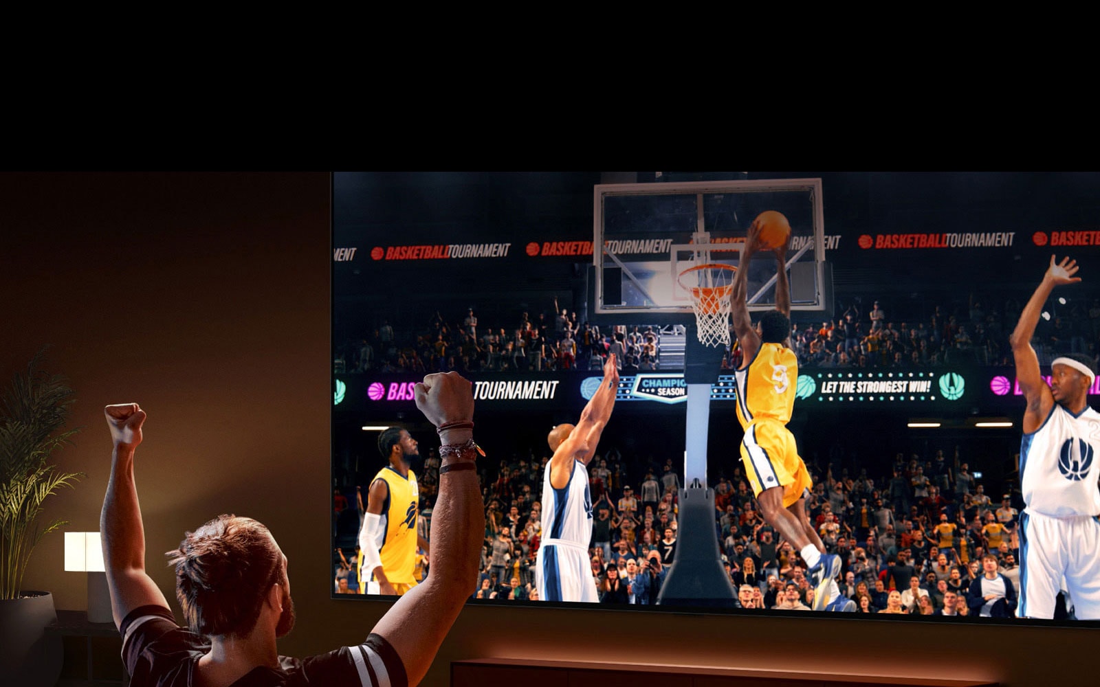 Čovjek sjedi na sofi ispred ultra velikog LG televizora  na kojem se prikazuje košarkaška utakmica, s rukama podignutim u zrak kao da navija.