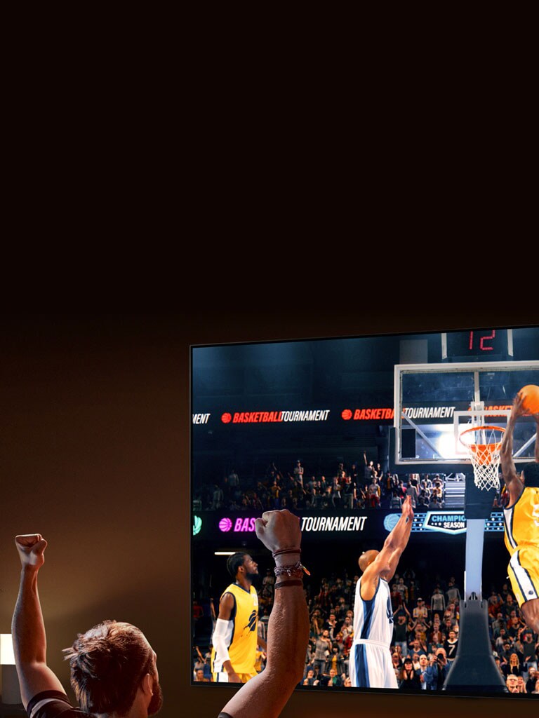 Čovjek sjedi na sofi ispred ultra velikog LG televizora  na kojem se prikazuje košarkaška utakmica, s rukama podignutim u zrak kao da navija.