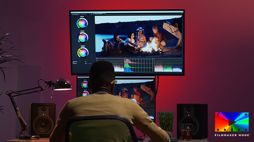 The director sits at a desk and uses two monitors to color-edit the video.