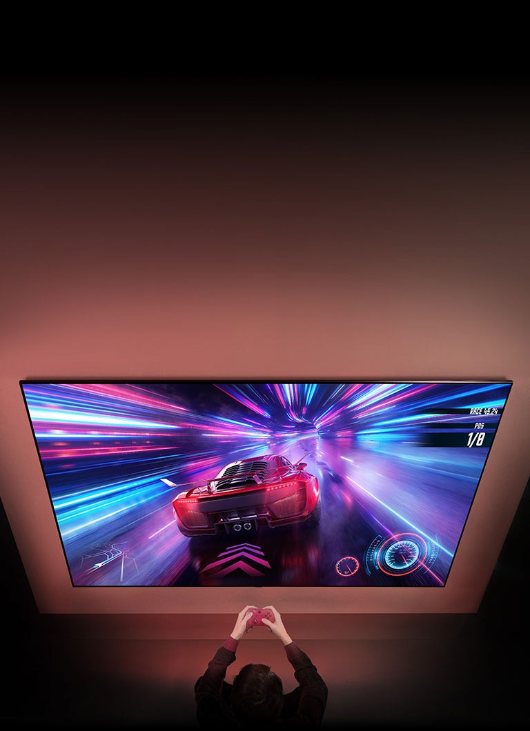 Veliki TV je na zidu i možete vidjeti zaslon trkaće videoigre na zaslonu. Ispred TV-a možete vidjeti ruke i upravljače osobe koja je fokusirana na igru.