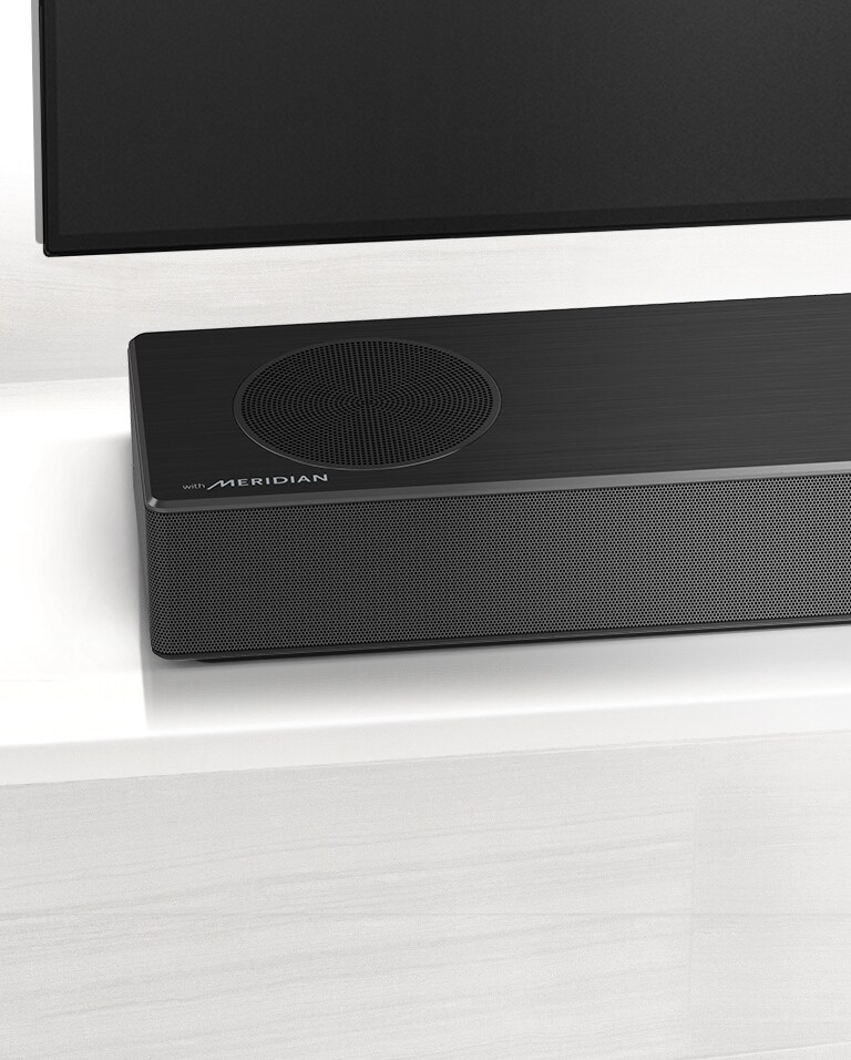 Prikaz izbliza lijeve strane zvučnika LG Soundbar s Meridianovim logotipom u donjem lijevom kutu. Vidljiva je i donja lijeva strana televizora.
