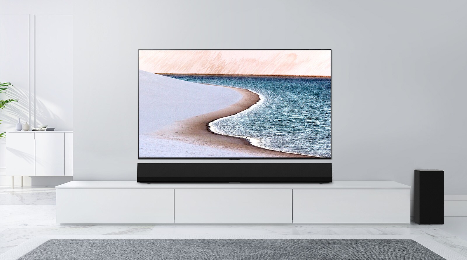 TV se montira na zid svjetlosive boje. LG Soundbar nalazi se ispod njega na bijelom ormariću. TV prikazuje plažu.