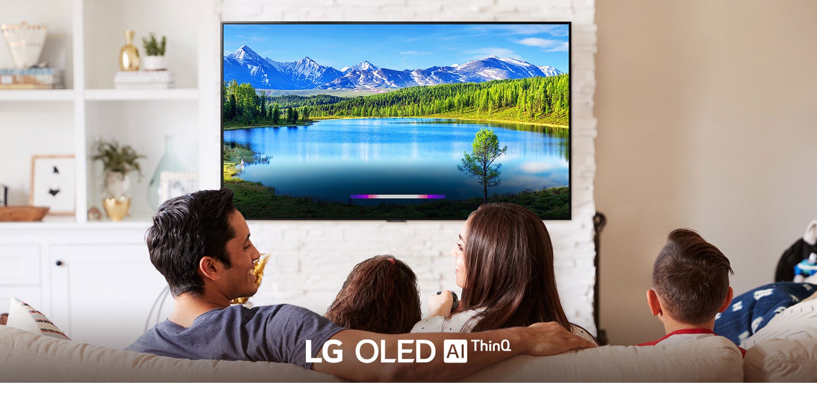 Obitelj u svijetloj dnevnoj sobi gleda krajolik na televizoru montiranom na zid