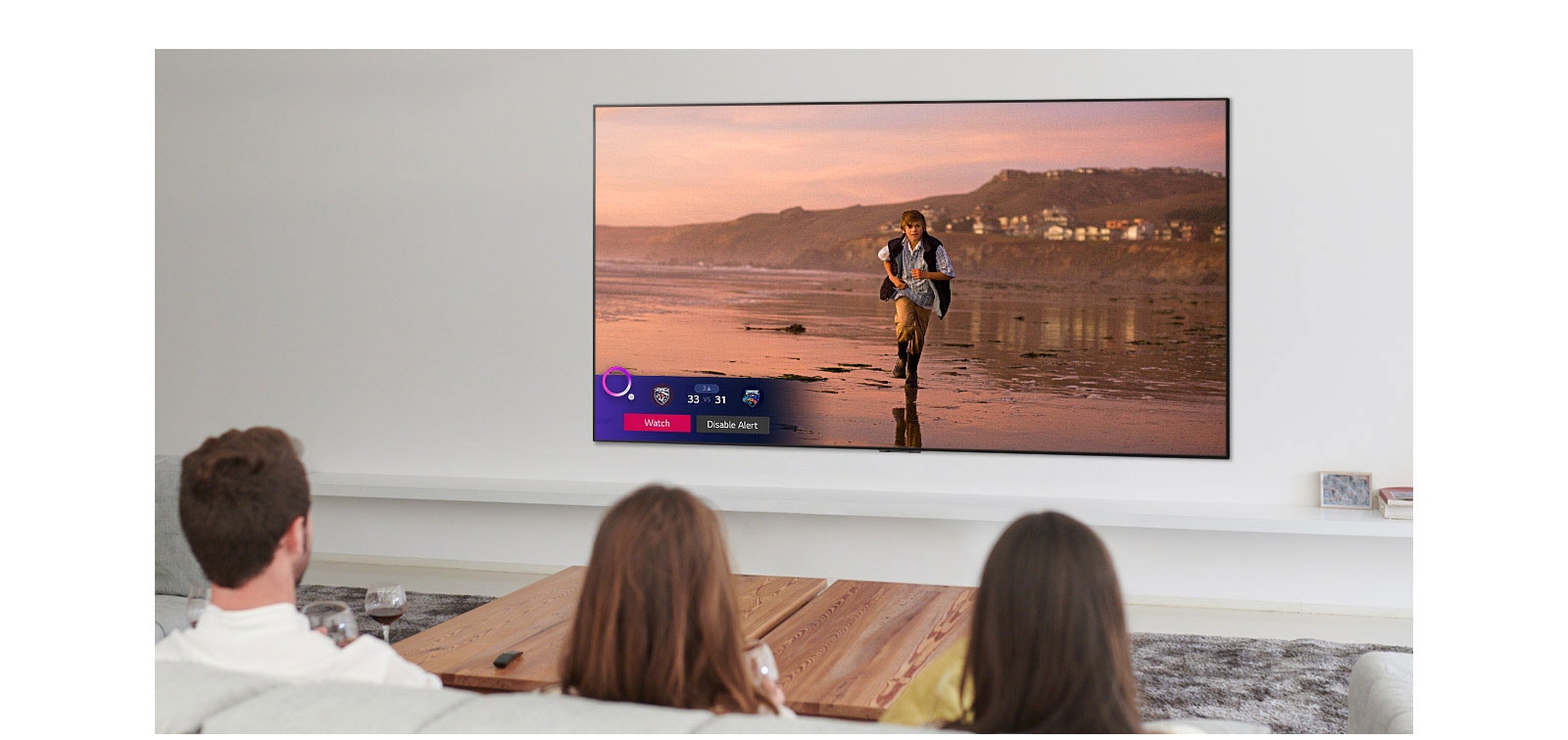 Troje ljudi koje gleda zaslon televizora na kojem je prikazana scena iz fantastičnog filma sa značajkom Sports Alert (Sportski podsjetnik)