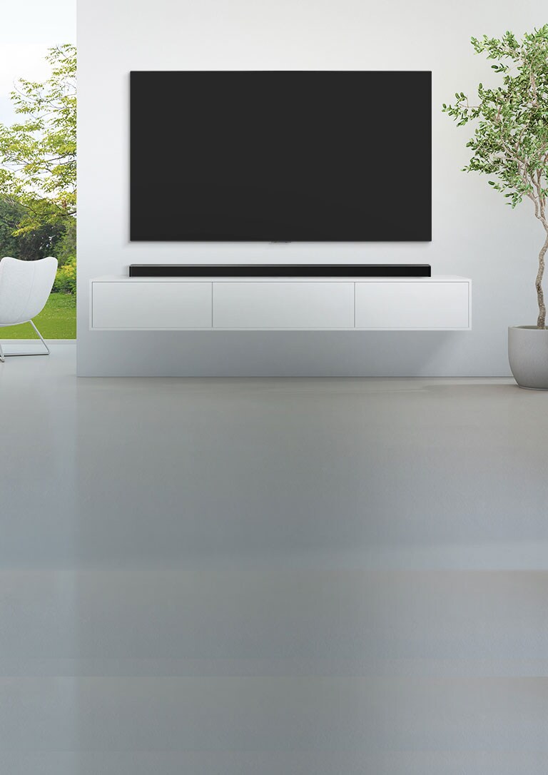 Televizor i zvučnik smješteni su u širokom, bijelom dnevnom boravku, a sa širokog se prozora pruža zeleni pogled na šumu.