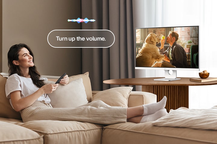 Žena pojačava glasnoću pametnog monitora LG Smart Monitor pomoću daljinskog upravljača Magic Remote.	