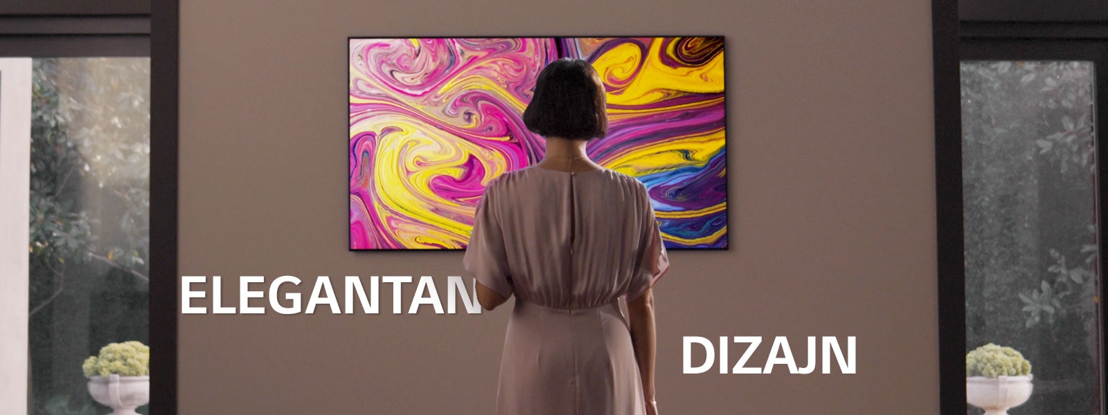 Žena gleda u televizor postavljen na zid na kojem se prikazuje umjetnička slika.