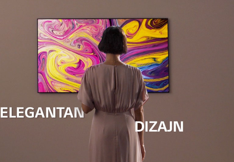 Žena gleda u televizor postavljen na zid na kojem se prikazuje umjetnička slika.