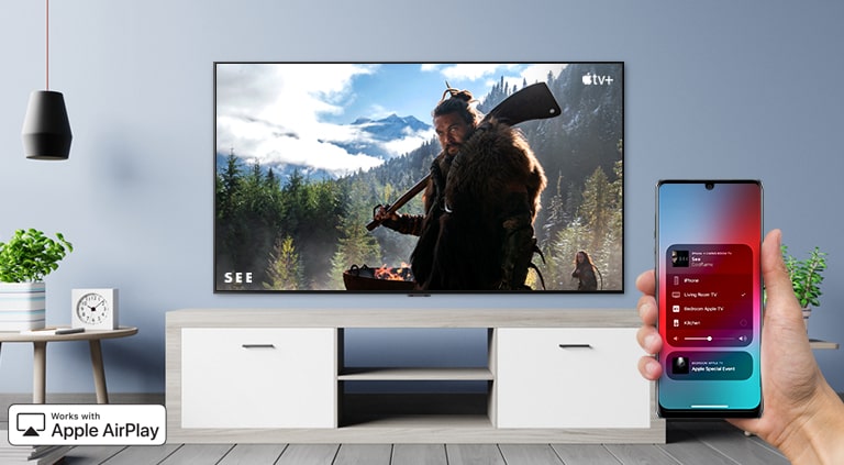 Prikaz izbliza ruke koja upravlja televizorom putem pametnog telefona iPhone i televizor koji prikazuje sadržaj Apple TV+.