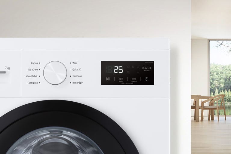 U pozadini je detalj sobe, a u prvom planu pogled izbliza na zaslon perilice rublja.