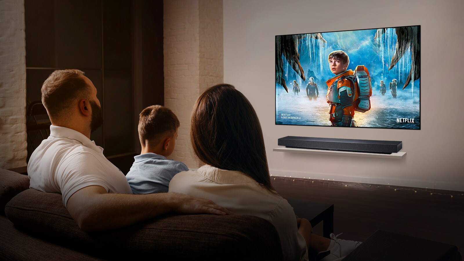 Par sjedi na sofi u dnevnoj sobi i gleda seriju LOST IN SPACE 2 na TV-u