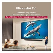 LG Televizor LG QNED AI QNED70 4K Smart TV 2025 od 55 inča, A family sits on a couch facing a LG QNED TV mounted on a wall above a LG Soundbar with a little girl pointing to a screen depicting two dolphins. The title talks about how every action is more thrill, 55QNED70A6A, thumbnail 7