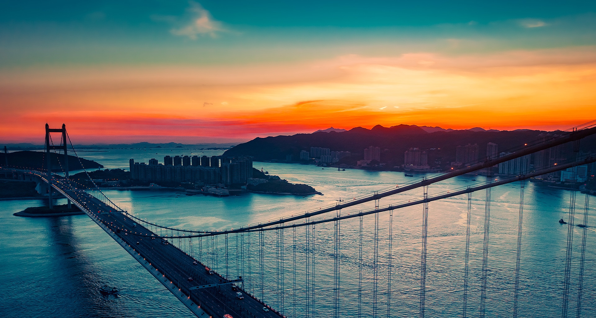 Pogled iz zraka na obalni grad s prometom koji vozi preko mosta dok sunce zalazi prikazuje se na cijelom zaslonu. Izrezan je i prikazan na televizijskom zaslonu LG OLED s nepromijenjenim izvornim bojama.