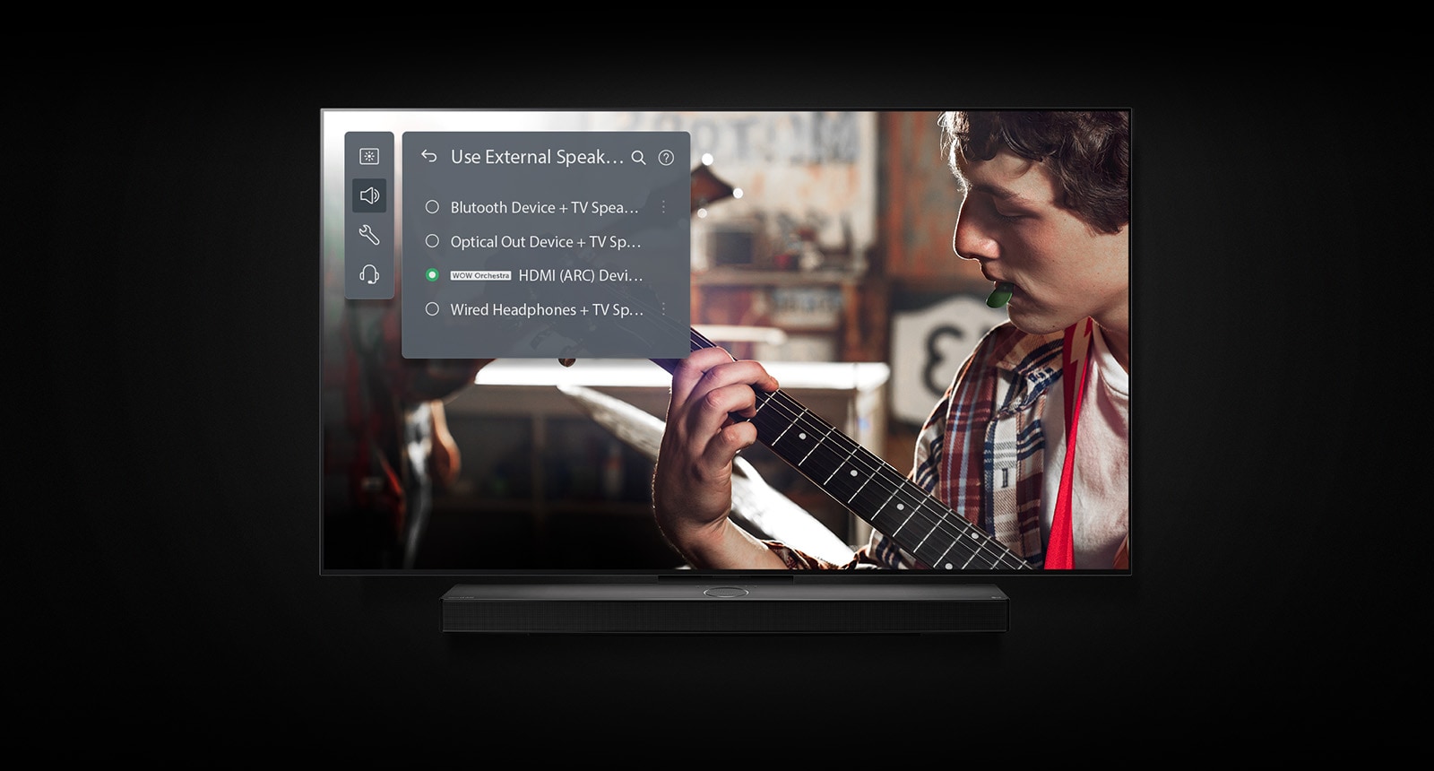 A képen az LG OLED TV látható egy hangprojektorral. A videóban egy fiú gitározik, fölötte pedig láthatók a hangprojektormód beállításai. 