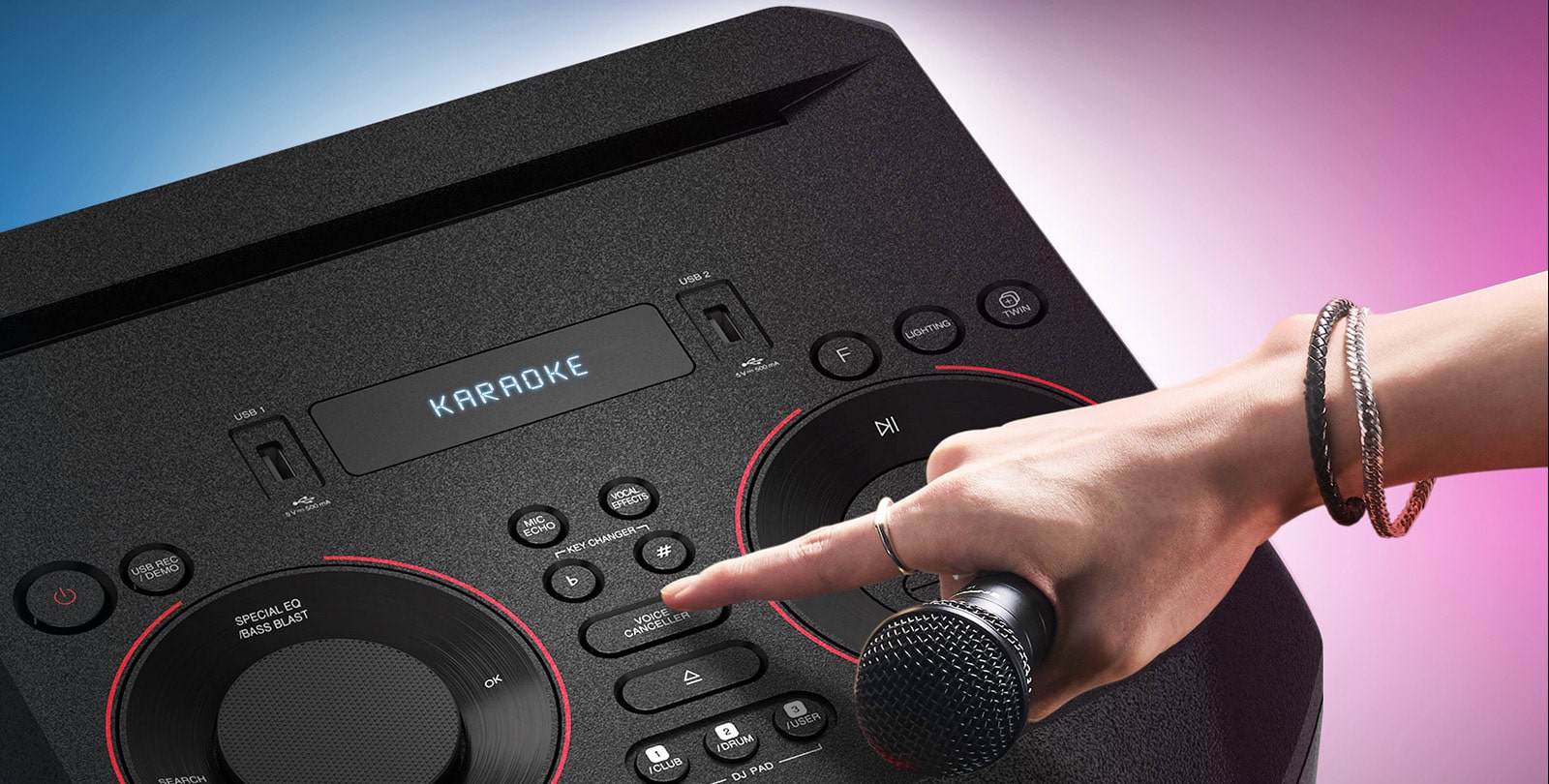 A hand holding a microphone tries to press the vocal mute button on the top of the LG XBOOM.