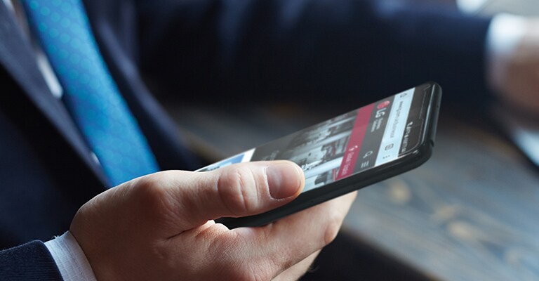 A képen egy ember egy okostelefont tart a kezében, amelynek képernyőjén az LG weboldala látható.