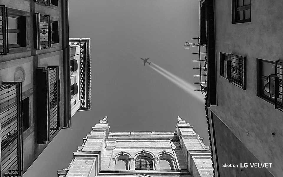 A black and white image of airplane flying through buildings shot on LG VELVET