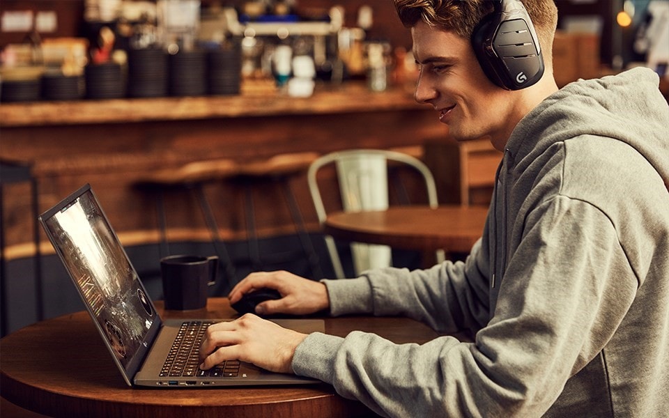 Egy fiatal férfi viselt heaphones játékok egy laptop egy kávézóban