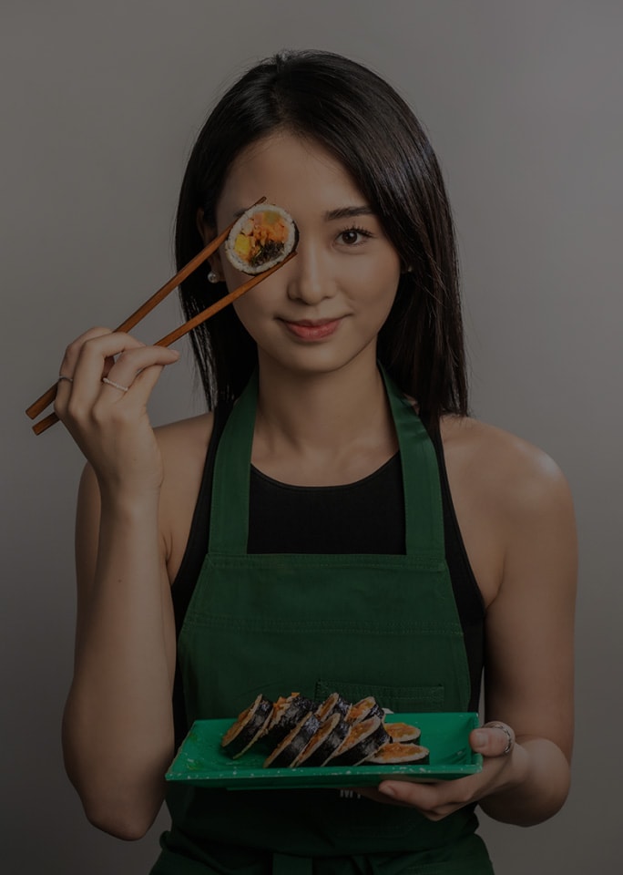 Tina Choi playfully holding a piece of kimbap near her eye.