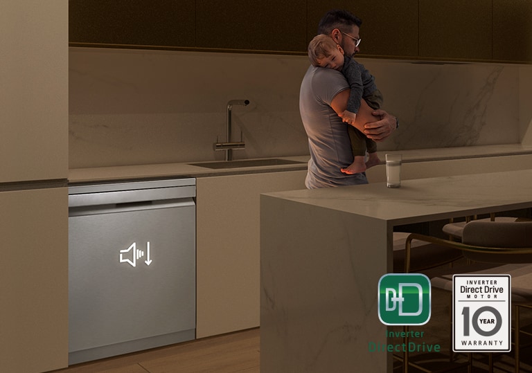 איש מחזיק תינוק ישן במטבח באור עמום, מדיח כלים רצפתי פועל בשקט ברקע.